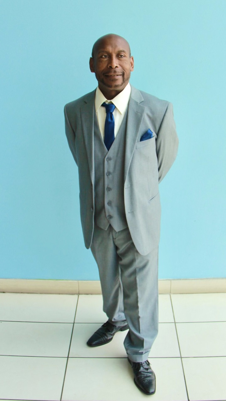 Robert Happyfeet Hernandez standing in a grey suit and blue tie